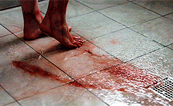 A person showering with bloody water running down the drain