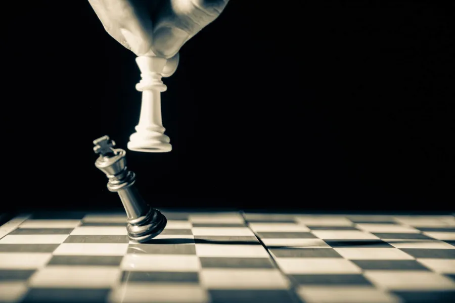 A person knocking down a queen while playing chess