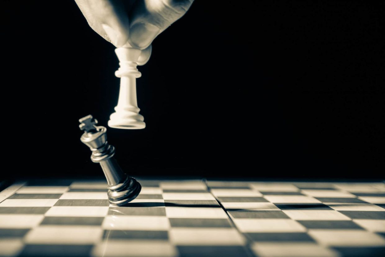 A person knocking down a queen while playing chess