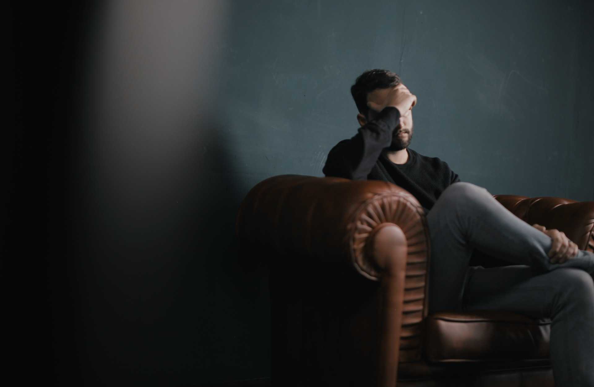 Man sitting down on a couch with his hand covering his face