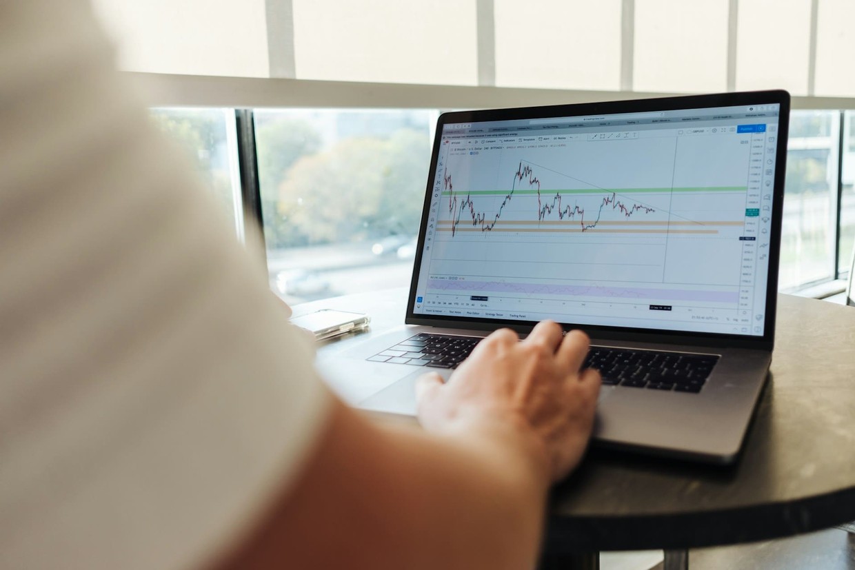 A day trader sitting at his desk with his laptop showing a marked up financial chart.