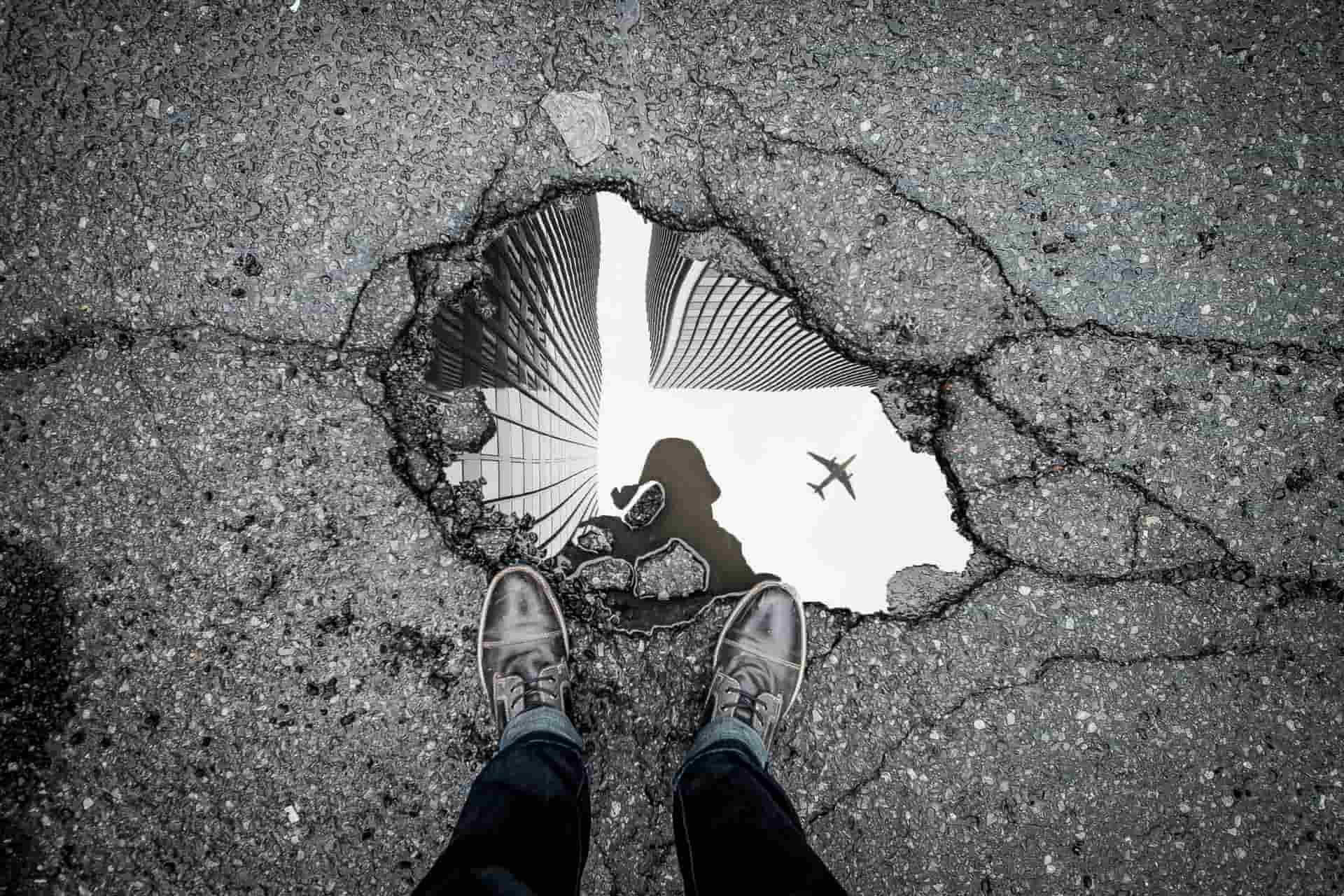 A man looking into a puddle and seeing his silhouette.