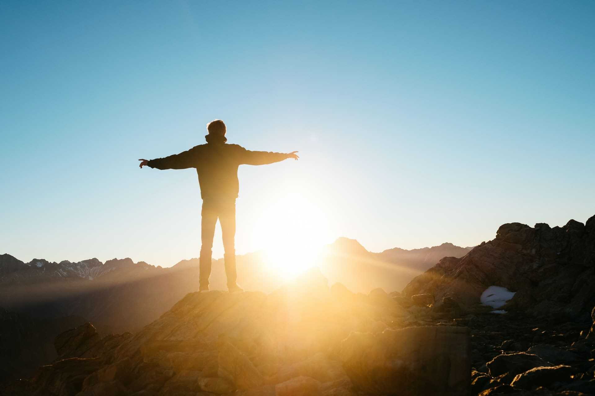 A man standing with his arms out as the sun rises.