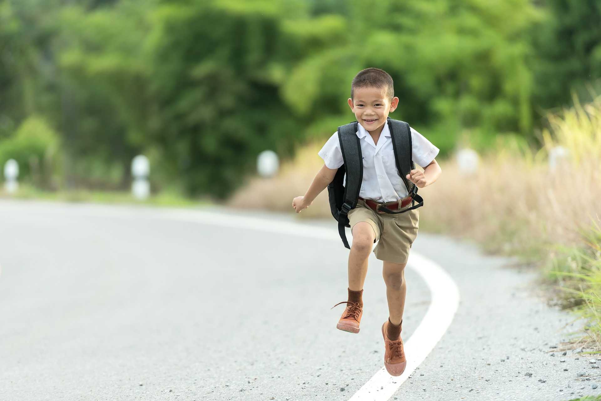 A boy with a backpack running down the street
